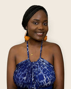Model wearring Zahara hand-woven amber raffia teardrop earrings by l'atelier kaay with an indigo adire halter dress.